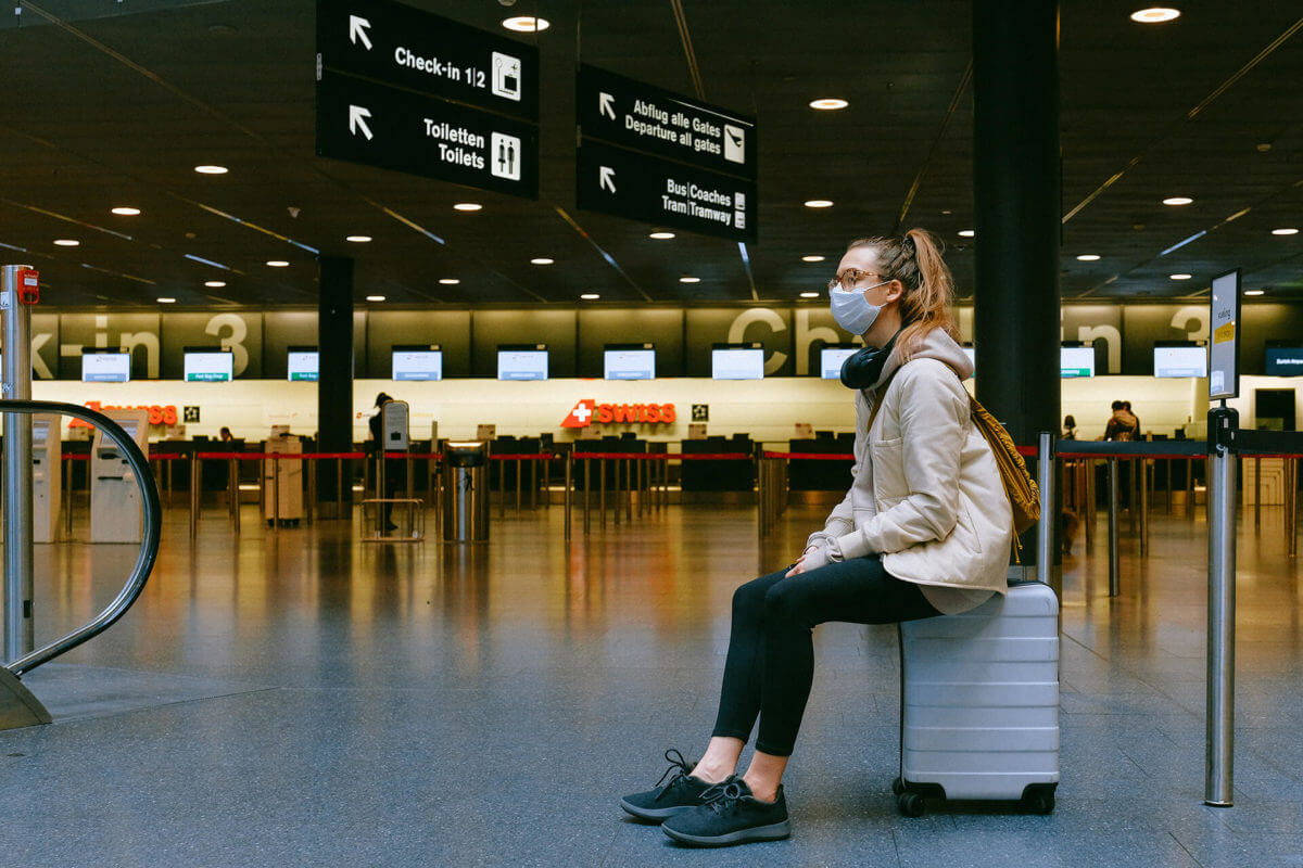A girl wearing a mask sitting on her suitcase at an airport