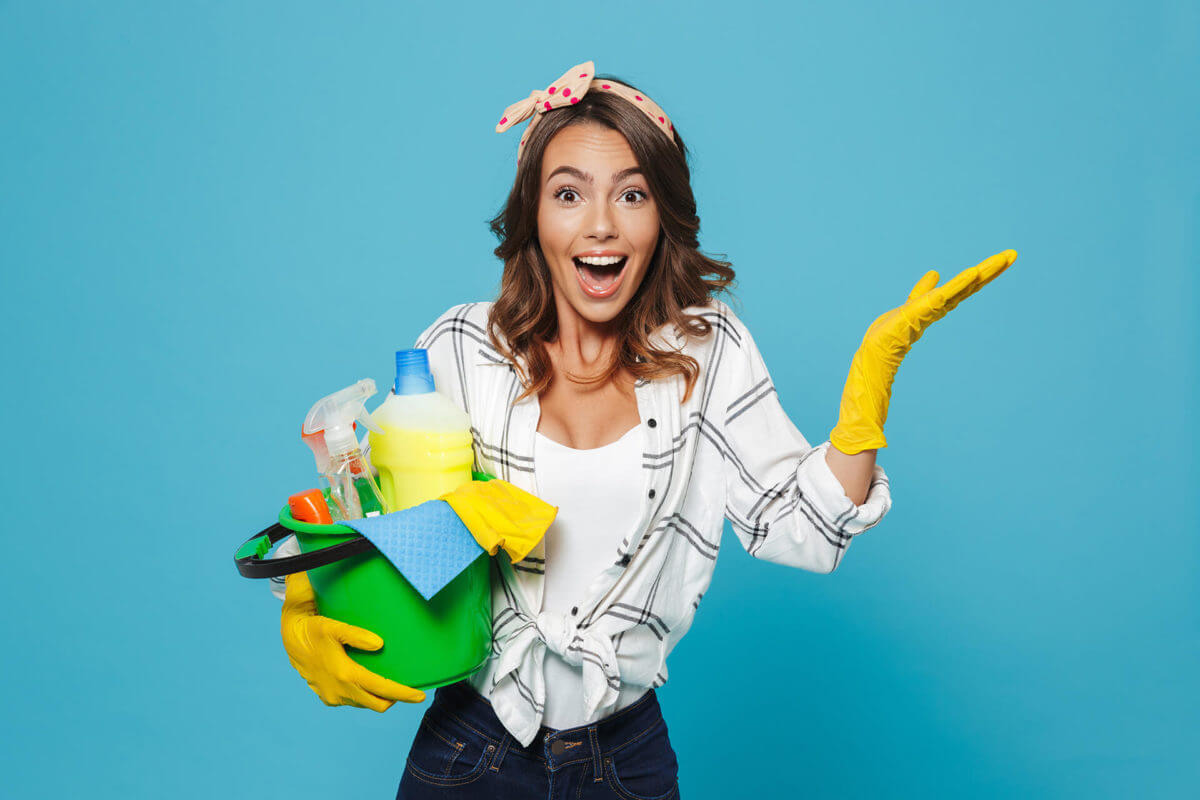 A girl wearing gloves holding a bucket full of cleaning supplies