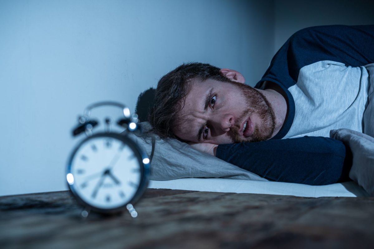 A man lying in bed trying to sleep while looking at a clock