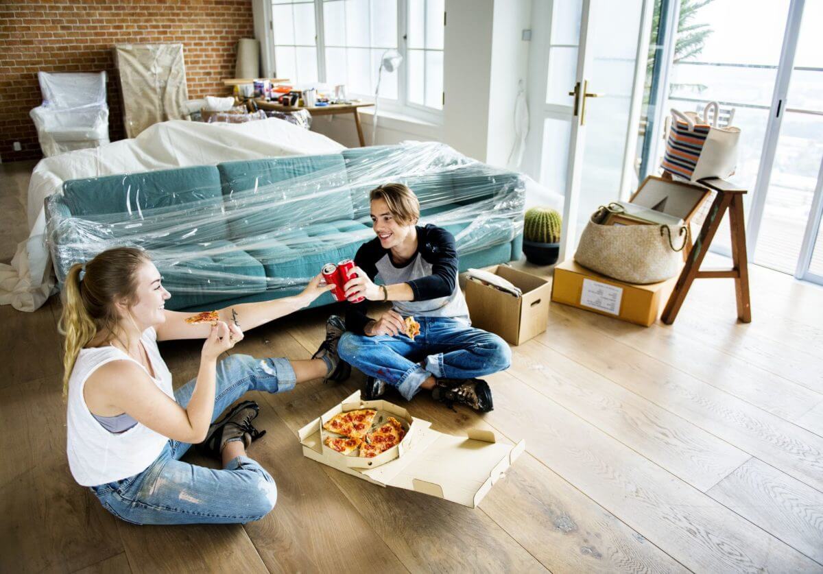 A girl and a boy sitting on the floor eating pizza after long-distance moving