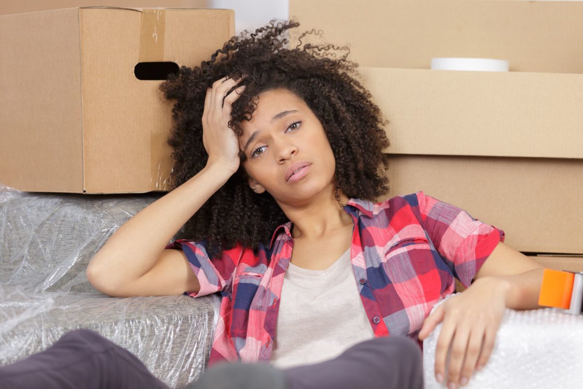 A worried girl holding her head and leaning on the pile of boxes after moving cross-country