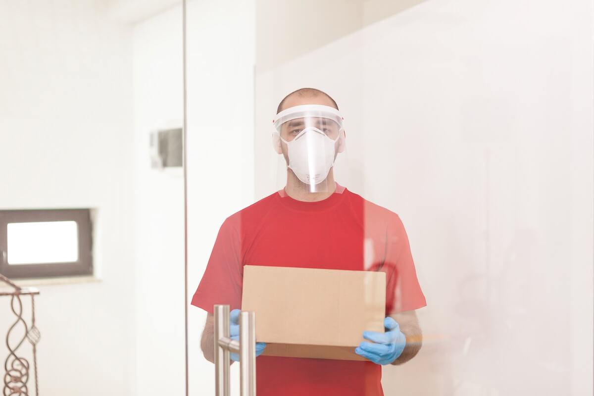 A person holding a box and wearing a mask and a protective visor