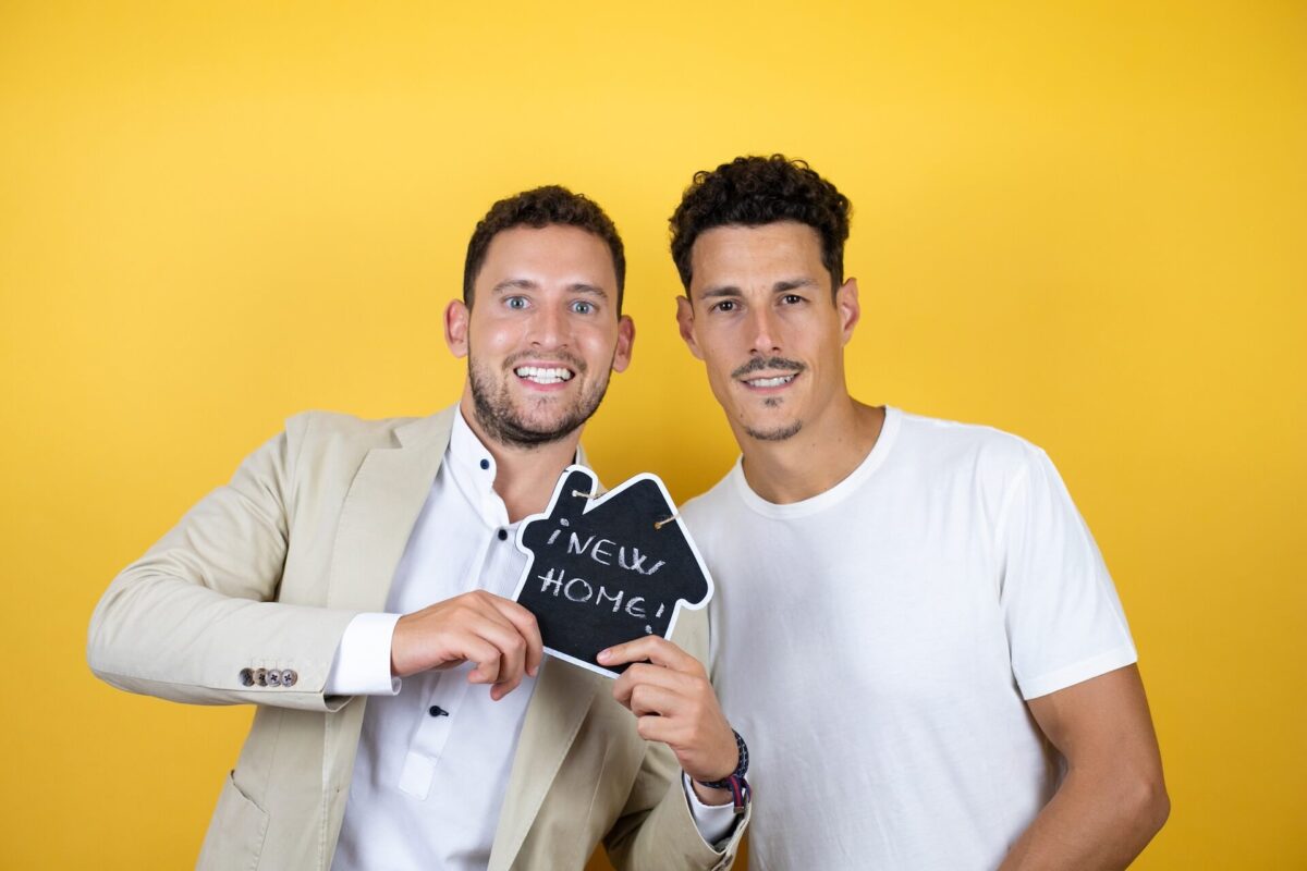 Two guys holding a 'new home' sign