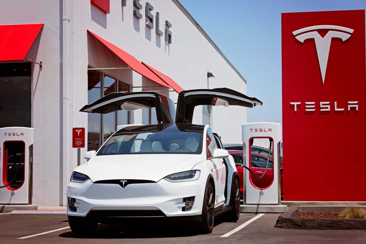 white tesla model x with falcon wing doors open charging at supercharger station