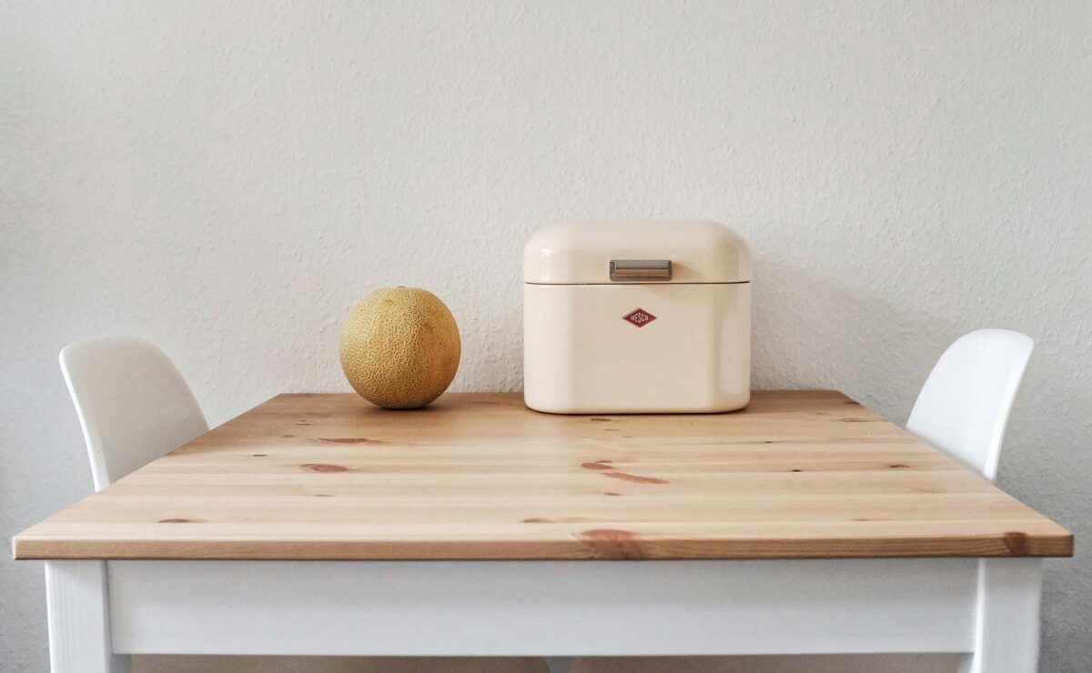 A wooden table with a melon and bread box on it