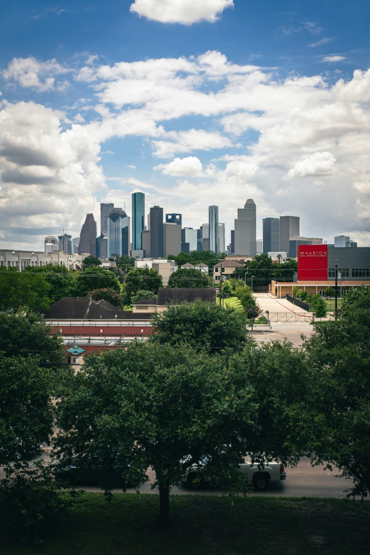 Lush green trees framing the modern downtown city skyline of Houston, Texas.